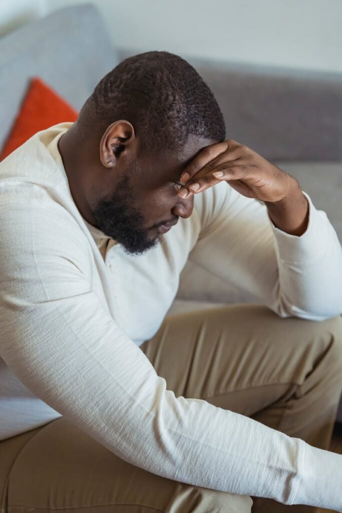 Side view of thoughtful African American male in casual clothes touching forehead and looking down